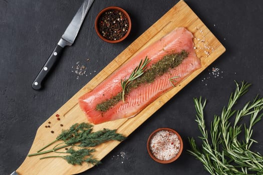 Salted fish fillet with spices and herbs:dill and rosemary on a wooden board on a black background.