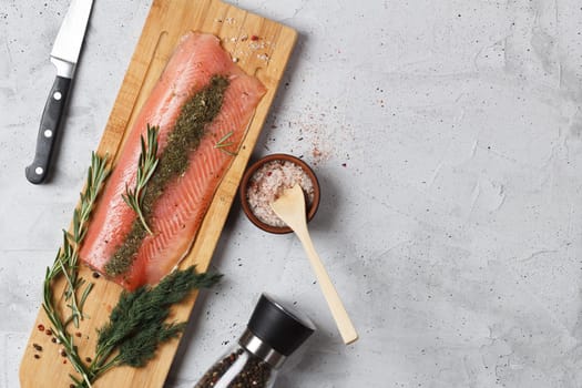 Salted fish fillet with spices and herbs: dill and rosemary on a wooden board on a gray background. copy space