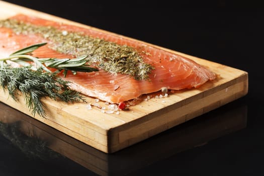 Salted fish fillet with spices and herbs:dill and rosemary on a wooden board on a black background.