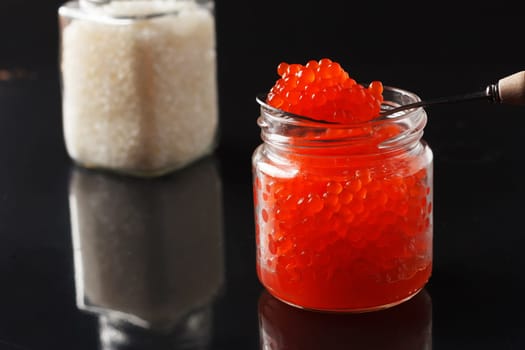 delicious red caviar in a glass jar and a jar of salt on a black background.