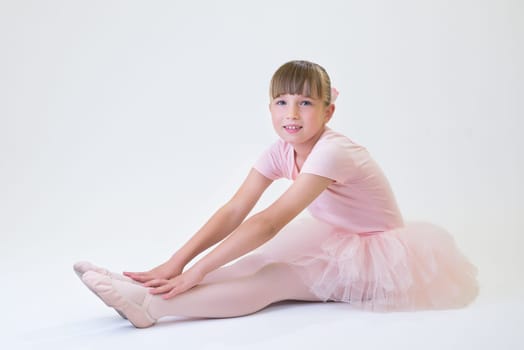 Little ballerina dancer in a pink tutu academy student posing on white background.