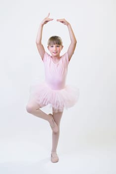 Little ballerina dancer in a pink tutu academy student posing on white background.