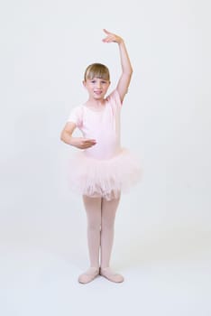 Little ballerina dancer in a pink tutu academy student posing on white background.