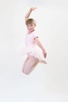 Little ballerina dancer in a pink tutu academy student posing on white background.