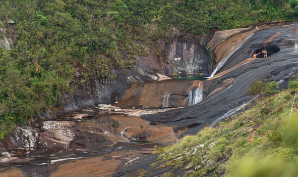 Long exposure shot of unrecognizable tourists taking photos for social media in the iconic spot of Caparao's valley with colorful water pools flowing over solid rock surrounded by jungle.