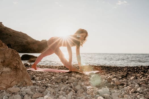 Young woman with black hair, fitness instructor in pink sports leggings and tops, doing pilates on yoga mat with magic pilates ring by the sea on the beach. Female fitness daily yoga concept