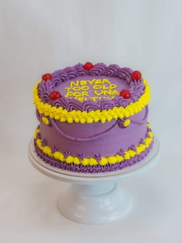 frosted icing violet yellow classic cilyndrical cake with text messagge topping on studio white background. Romantic layered cupcake.