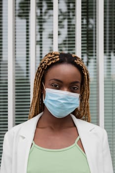 Portrait of african american young woman looking at camera wearing a protective face mask. Vertical image. Health care concept.