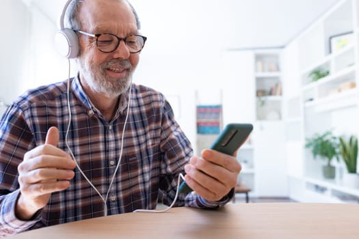 Senior man listening to music and dancing using mobile phone and headphones at home living room. Technology and lifestyle concept.