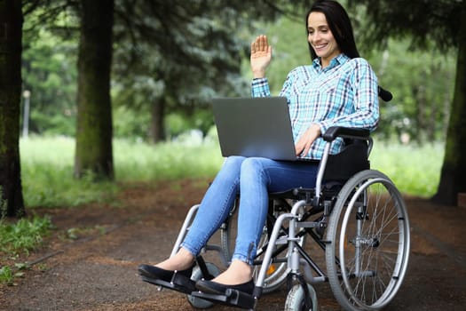 Woman with laptop works in wheelchair in park. Remote work and education for people with disabilities