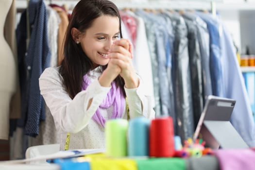 Smiling female seamstress stylist talking on video call on tablet. Remote communication with customers in studio