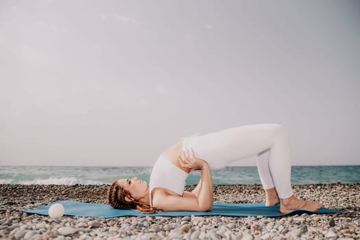 Woman yoga sea. Well looking middle aged woman with braids dreadlocks in white leggings and tops doing stretching pilates on yoga mat near sea. Female fitness yoga routine concept. Healthy lifestyle