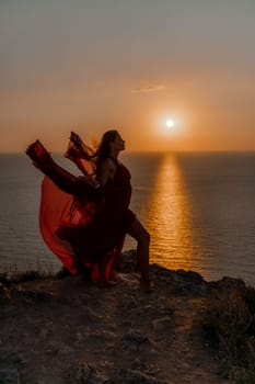 Woman sunset sea red dress, back view a happy beautiful sensual woman in a red long dress posing on a rock high above the sea on sunset