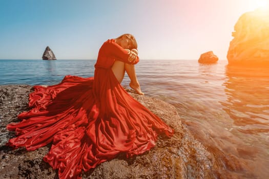 woman sea red dress. Beautiful sensual woman in a flying red dress and long hair, sitting on a rock above the beautiful sea in a large bay