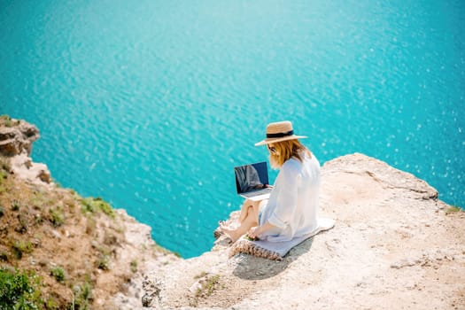 Freelance woman working on a laptop by the sea, typing away on the keyboard while enjoying the beautiful view, highlighting the idea of remote work