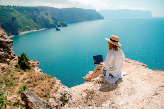 Freelance woman working on a laptop by the sea, typing away on the keyboard while enjoying the beautiful view, highlighting the idea of remote work