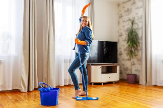 Funny happy young woman with mop singing, dancing and having fun while cleaning floor. Housewife enjoying domestic chores, doing home cleanup creatively
