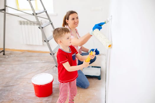 Happy family mother and child son paint the wall with paint using roller and brush. Repair in the apartment