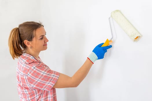 Happy woman with roller painting wall in her new apartment. Renovation, redecoration and repair concept