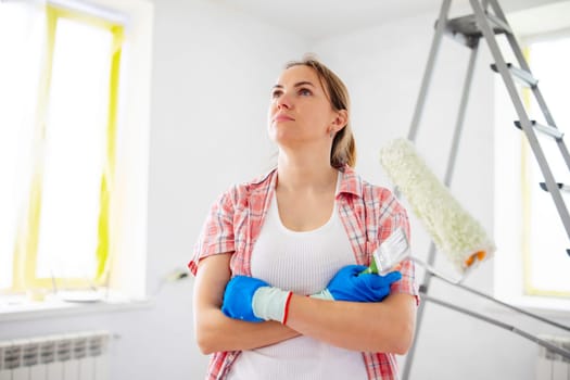 People renovation and home improvement. Positive satisfied woman holding dirty roller and brush after painting walls in room