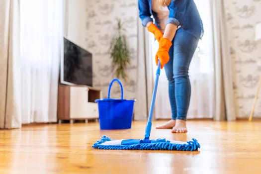 Cropped image of young woman in casual clothes washing a wooden floor with a damp microfiber mop, doing homework, routine cleaning, cleaning job concept