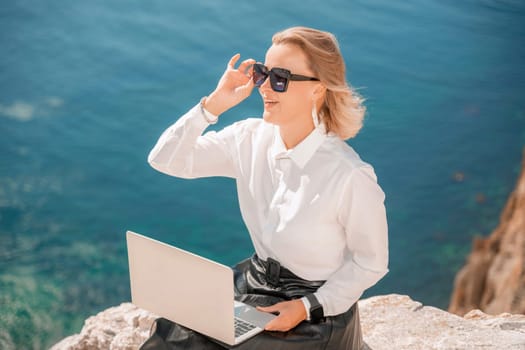 Business woman on nature in white shirt and black skirt. She works with an iPad in the open air with a beautiful view of the sea. The concept of remote work