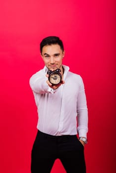 Emotional young man holding clock on a red background. Being late concept