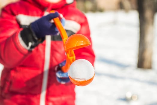 A device for sculpting snowballs in childrens hands against a background of snow. Childrens winter games of snowballs.