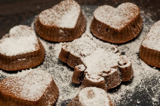 Delicious chocolate muffins or cupcakes in powdered sugar on black plate on dark wooden background. Homemade bakery.