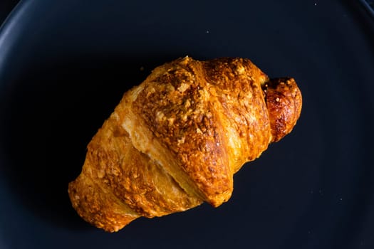 Freshly backed french croissant shiny in the rays of morning sun, dark background, kitchen