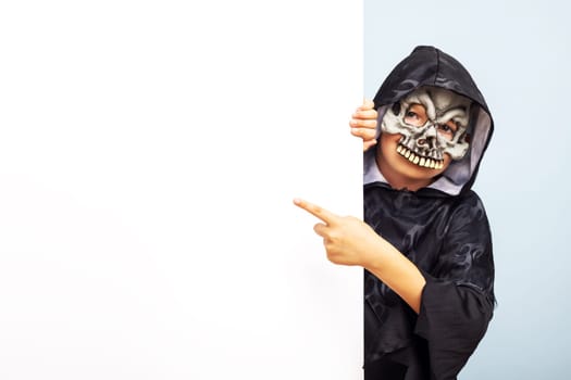 Happy Halloween. Cute little boy in a costume hiding behind white banner blank. Happy kid holding cardboard background with copy space.