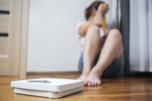 White scale and depression, upset and sad woman with measuring tape on wooden floor.