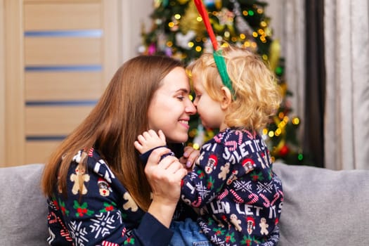 Child kissing and hugging his mother on the couch in front of the christmas tree. Marry Christmas.