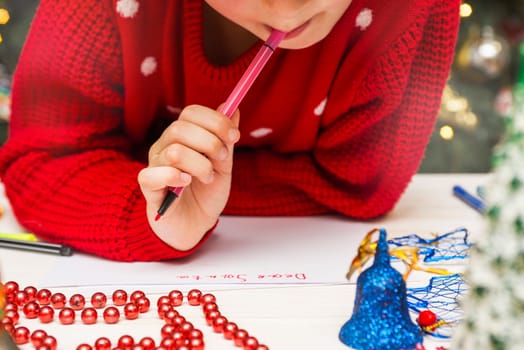 Little boy in a red sweater writes letter to Santa Claus. Christmas Child writing wish list.