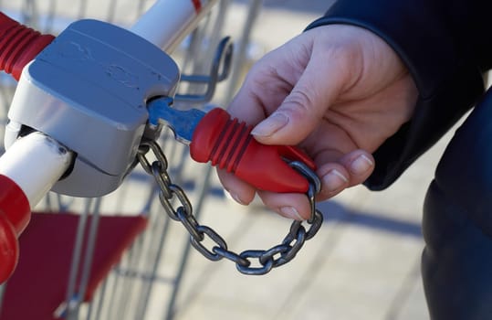 A woman's hand inserts a key into the lock of a grocery cart. Shopping in the store. Transportation of goods.