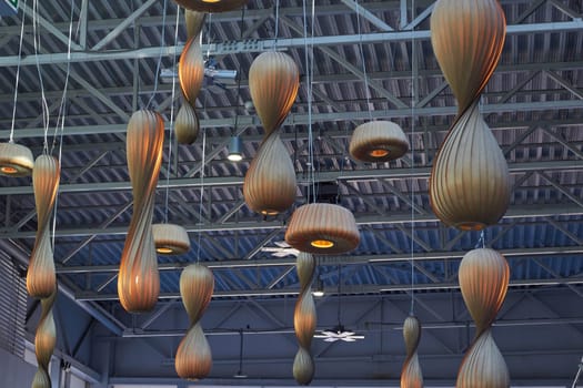 Large wooden lamps hanging from the ceiling. Metal Ceiling of the shopping center. Lighting of shops.