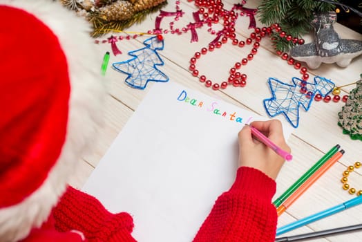 Little boy in Santa hat writes letter to Santa Claus. Kid in Santa hat writing wish list