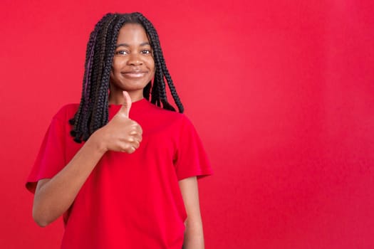 Happy african woman gesturing agreement raising a thumb up in studio with red background