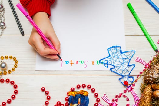 Little child writes letter to Santa. Kids hand with felt-tip pen writes a letter to Santa. Wishlist