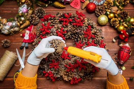 Creating a Christmas wreath with womens hands on a wooden background. Concept of preparation for Christmas and New Year. Decoration for the house for Christmas.