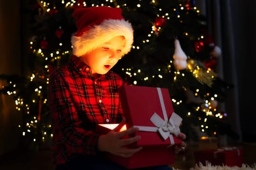 Cute little boy opening magic Christmas gift by a Christmas tree in cozy living room in winter. Merry Christmas