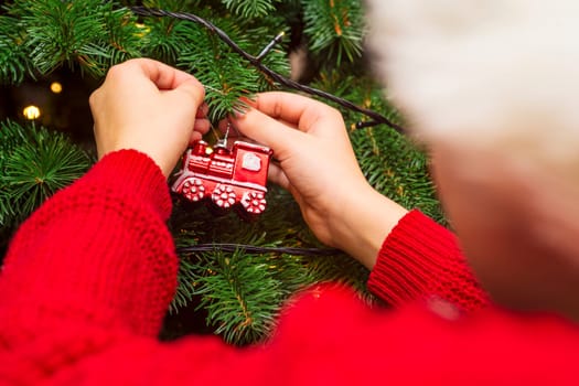 A child in Santa hat is decorating Christmas tree with toys and baubles. A kid preparing home for xmas celebration.