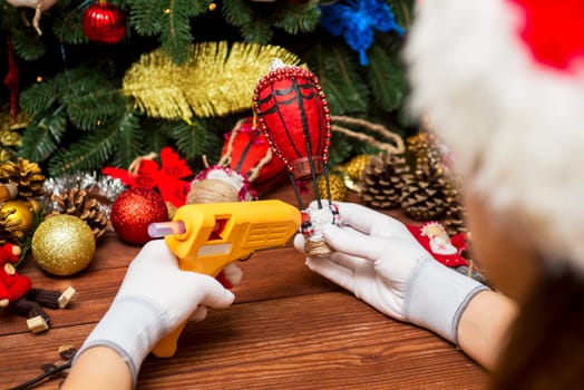 Female hands white gloves with a glue gun make Christmas decorations or toys. Making New Year decoration. Christmas ornaments.