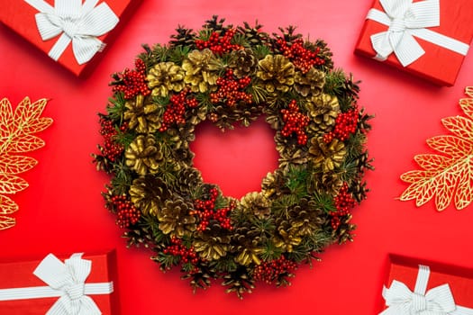 Christmas composition. Christmas background with fir and cones wreath, christmas presents, golden leaves on red background. Flat lay, top view.