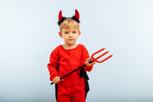 Happy Halloween. Cute little boy in devil halloween costume with horns and trident on light blue background.