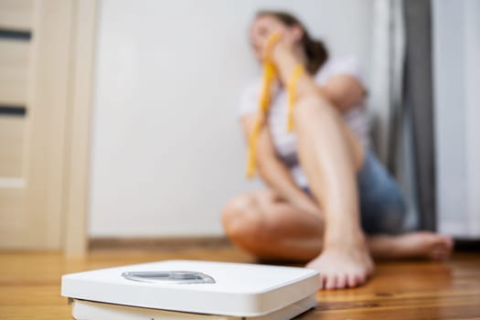 White scale and depression, upset and sad woman with measuring tape on wooden floor.