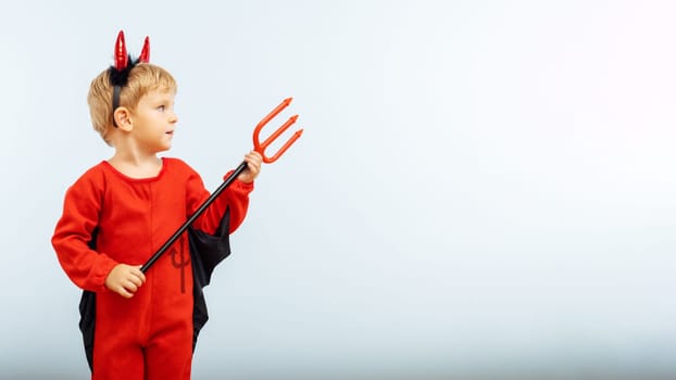 Happy Halloween. Cute little boy in devil halloween costume with horns and trident on light blue background.