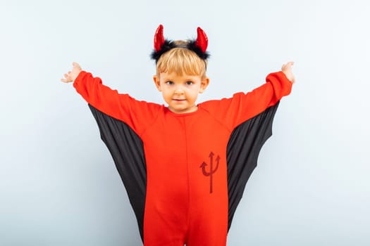Happy Halloween. Cute little boy in devil halloween costume with horns on light blue background.