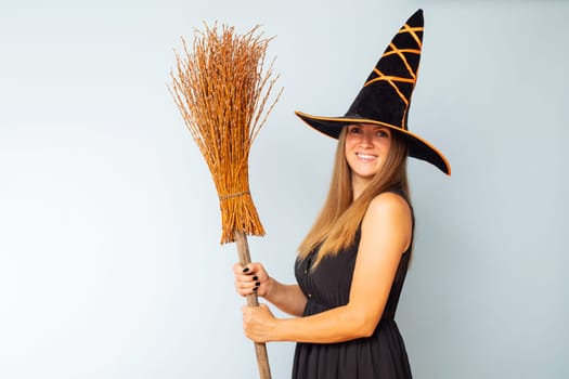 Happy Halloween. Happy young woman in halloween witch costume with broom on a light background. Halloween party concept.