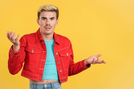 Astonished gay man gesturing and looking at the camera in studio with yellow background